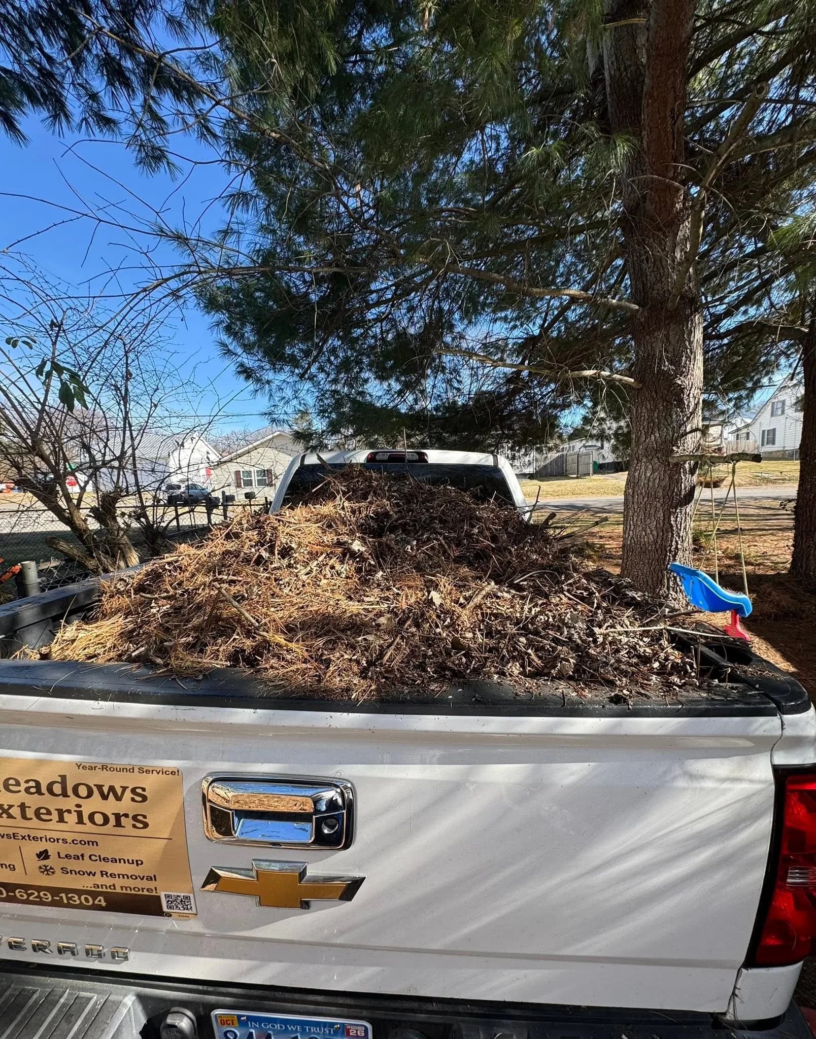 White Meadows Exteriors pickup truck loaded with branches and brush beneath a large tree.